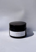 Product photography of a black glass jar of SOS 4:7 Organic Whipped Beef Tallow Moisturizer on a light grey surface, featuring a white label with reddish-brown text and a subtle leaf design, casting a soft shadow